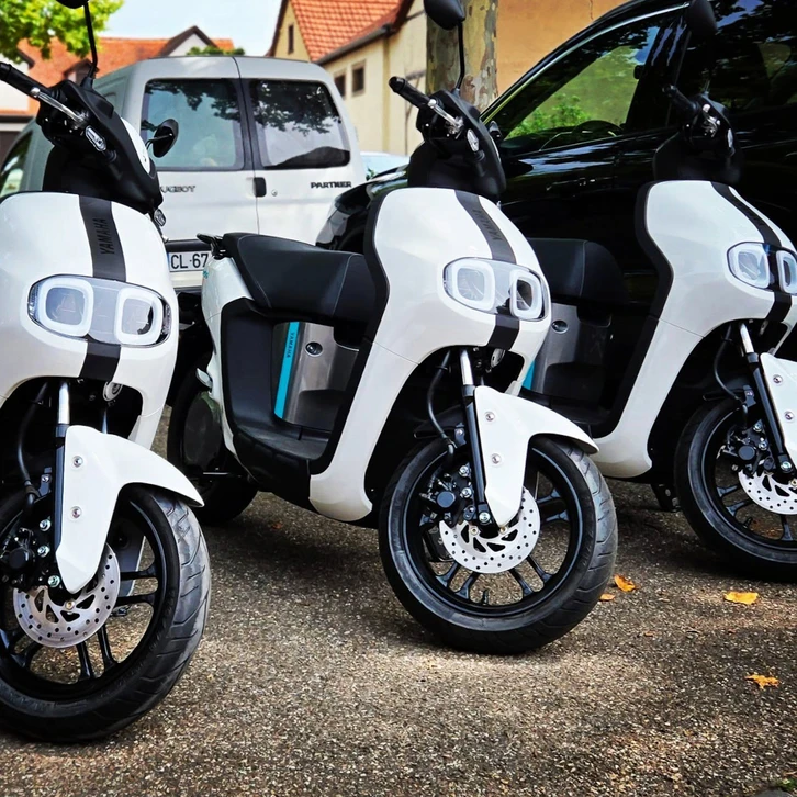 Moniteur expérimenté donnant une instruction de conduite à un élève motocycliste en équipement de protection complet, dans un environnement de formation en Alsace. Le moniteur se tient à proximité, observant attentivement la conduite de l'élève avec une attitude pédagogique et bienveillante. La scène se déroule sur une route de conduite pédagogique en conditions réalistes, montrant l'accompagnement personnalisé et le savoir-faire transmis aux conducteurs en formation.