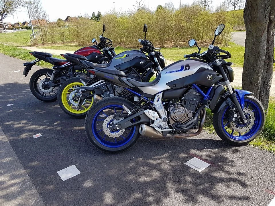 Photographie d'une moto standard rabaissée (de type scooter ou moto légère) stationnée en atelier ou espace de formation, avec un élève de petite stature assis confortablement dessus, les deux pieds posés à plat au sol, portant un casque et équipement de protection adéquat, illustrant l'accessibilité et la sécurité pédagogique de la formation motocycliste pour tous les gabarits.